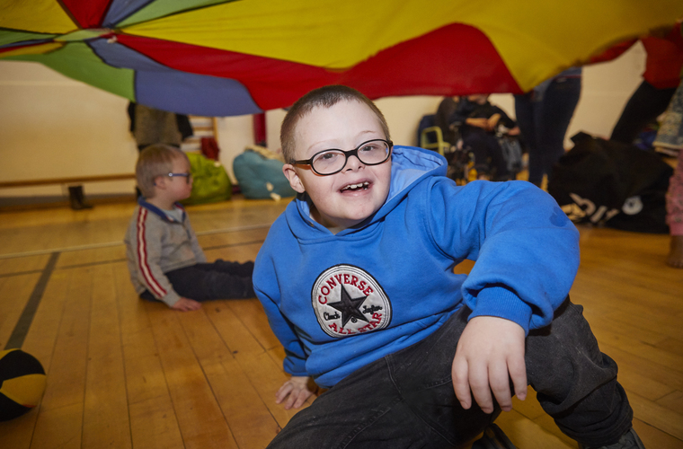 Young boy takes part in a group activity with a rainbow parachute in a sports hall