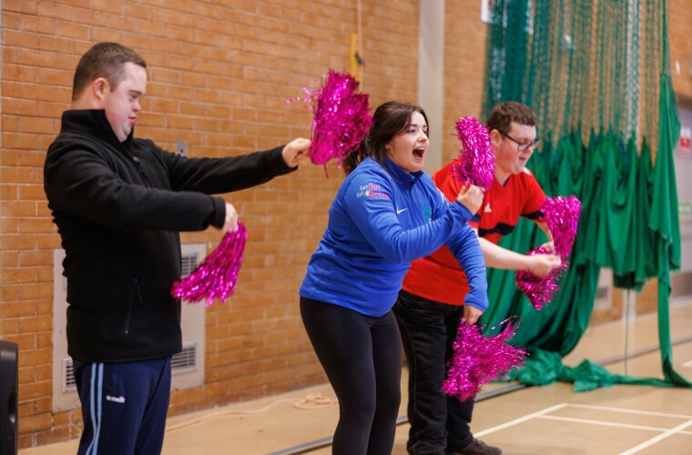 Group of disabled and non-disabled people taking part in a dance session using pom poms. 