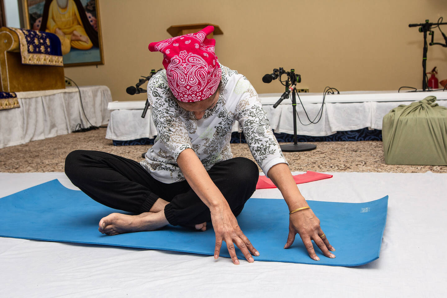A woman sits on a yoga mat stretching forward. 