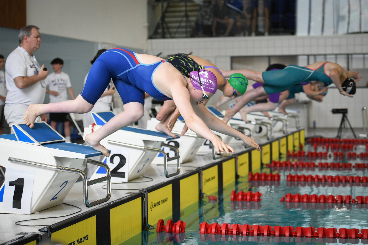 Swimmers dive into a pool off starting blocks. 