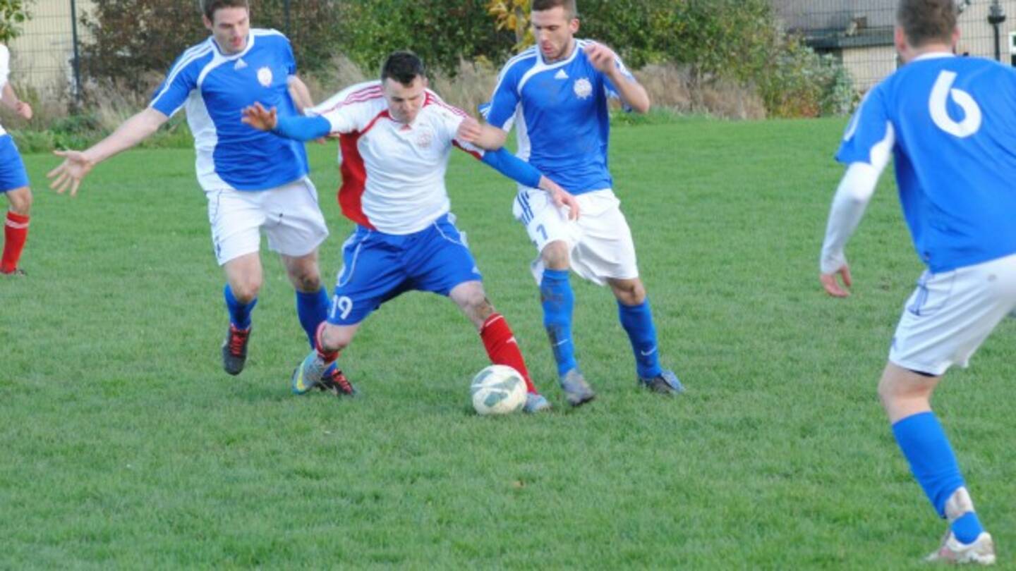 A group of men with hearing impairments are playing a game of football. The men are dressed in blue shirts and they are playing on a grass pitch.