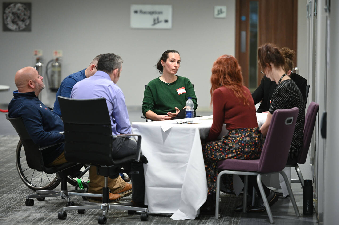 A group of people sit around a table in a conference centre setting.