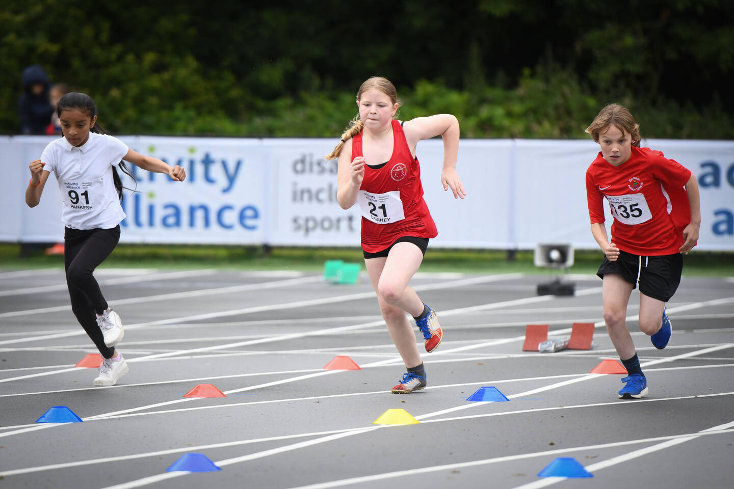 Two girls and a boy run on a running track.