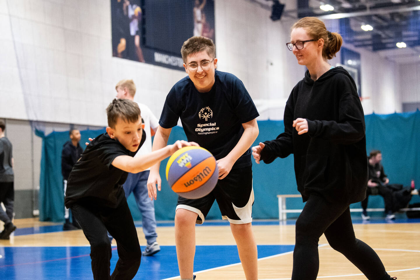 Two boys and a girl chase a basketball on a court.