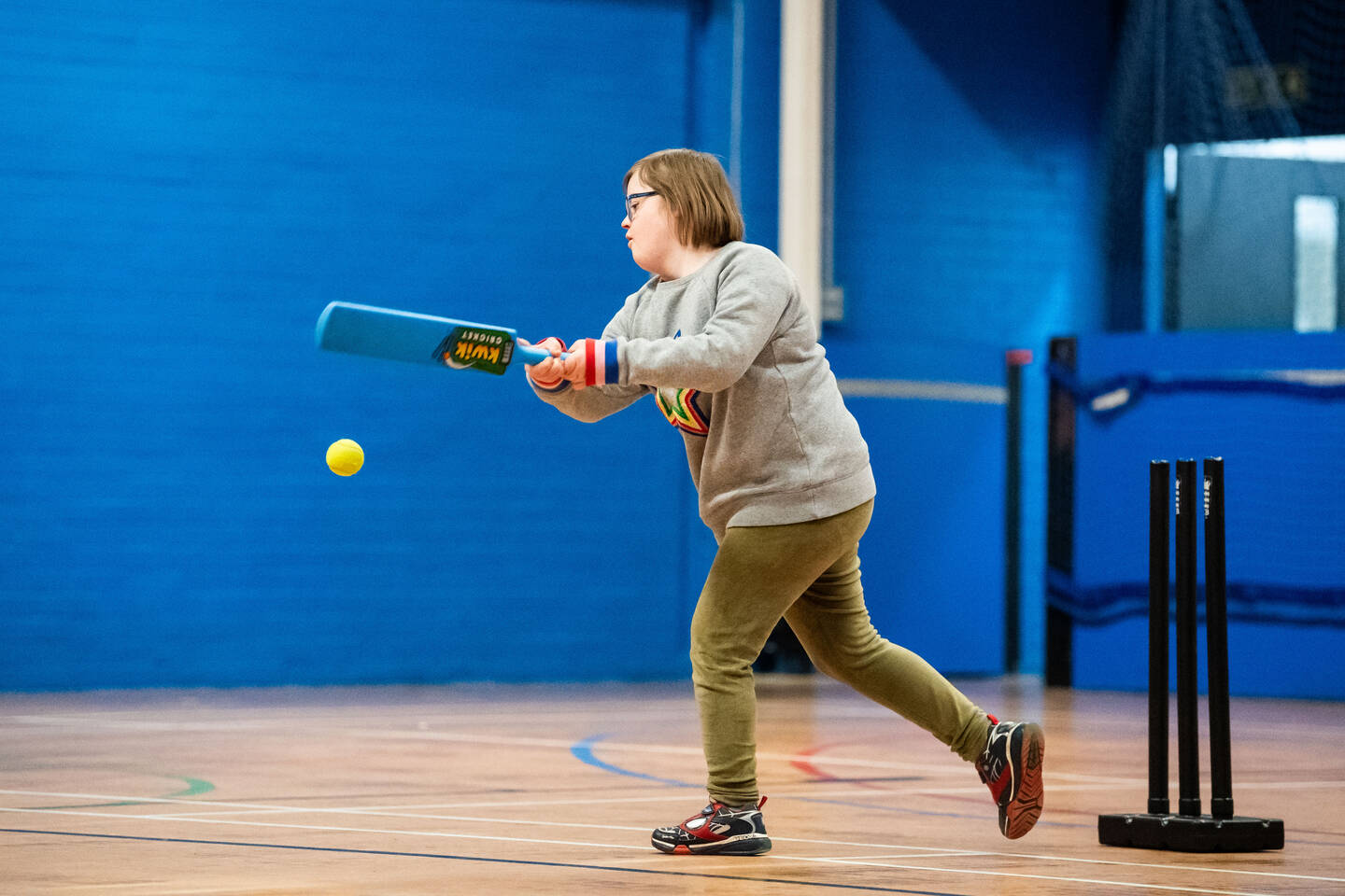 A girl plays a cricket shot in a sports hall.