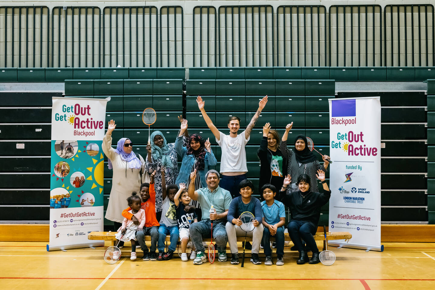 A group of people cheer in a sports hall. There are banners alongside them with the Get out Get Active logo on them.