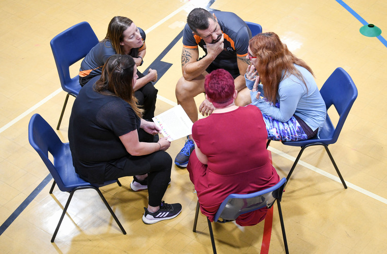 Group of people sat in a circle in a sportshall chatting