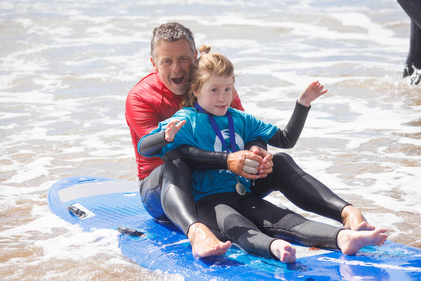 A man and a young girl sit together on a surfboard in the sea
