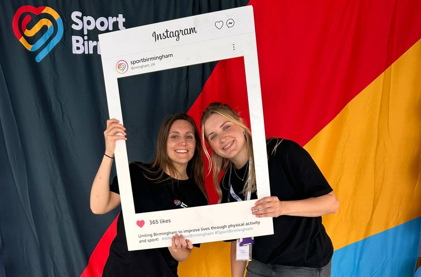 Ali and a colleague smile behind a social media board.