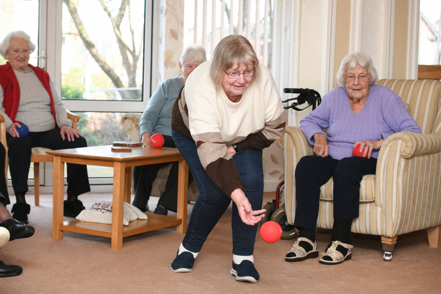 A woman bowls a ball in a room with people sitting watching.