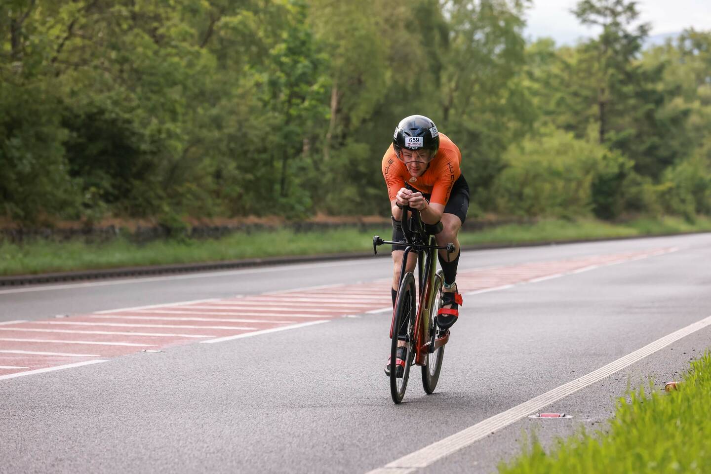 Oliver Pritchard in a cycling racing suit on a road bike cycles on a road.