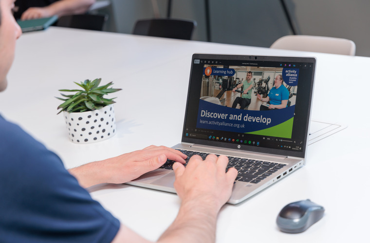 A man sits at a laptop looking at the Activity Alliance website
