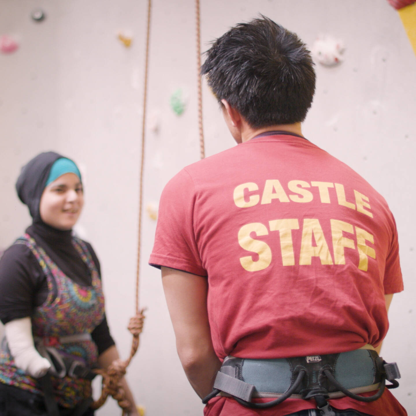 A staff member stands in front of a woman at a climbing wall.