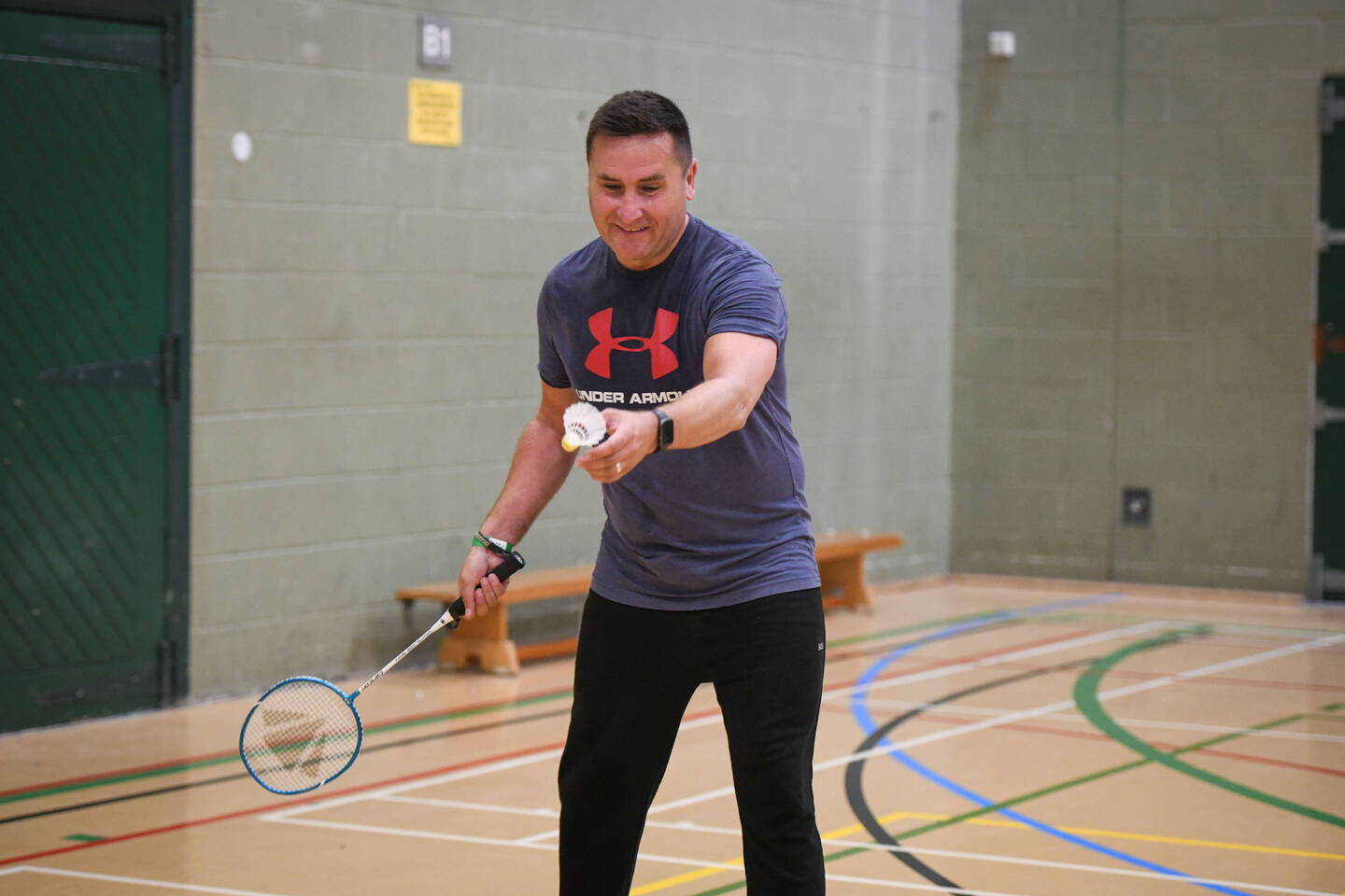 A man hits a shuttlecock with a badminton racquet in a sports hall.