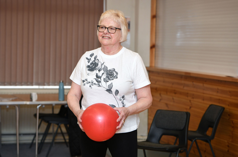 Older woman holds a red ball during a fitness class