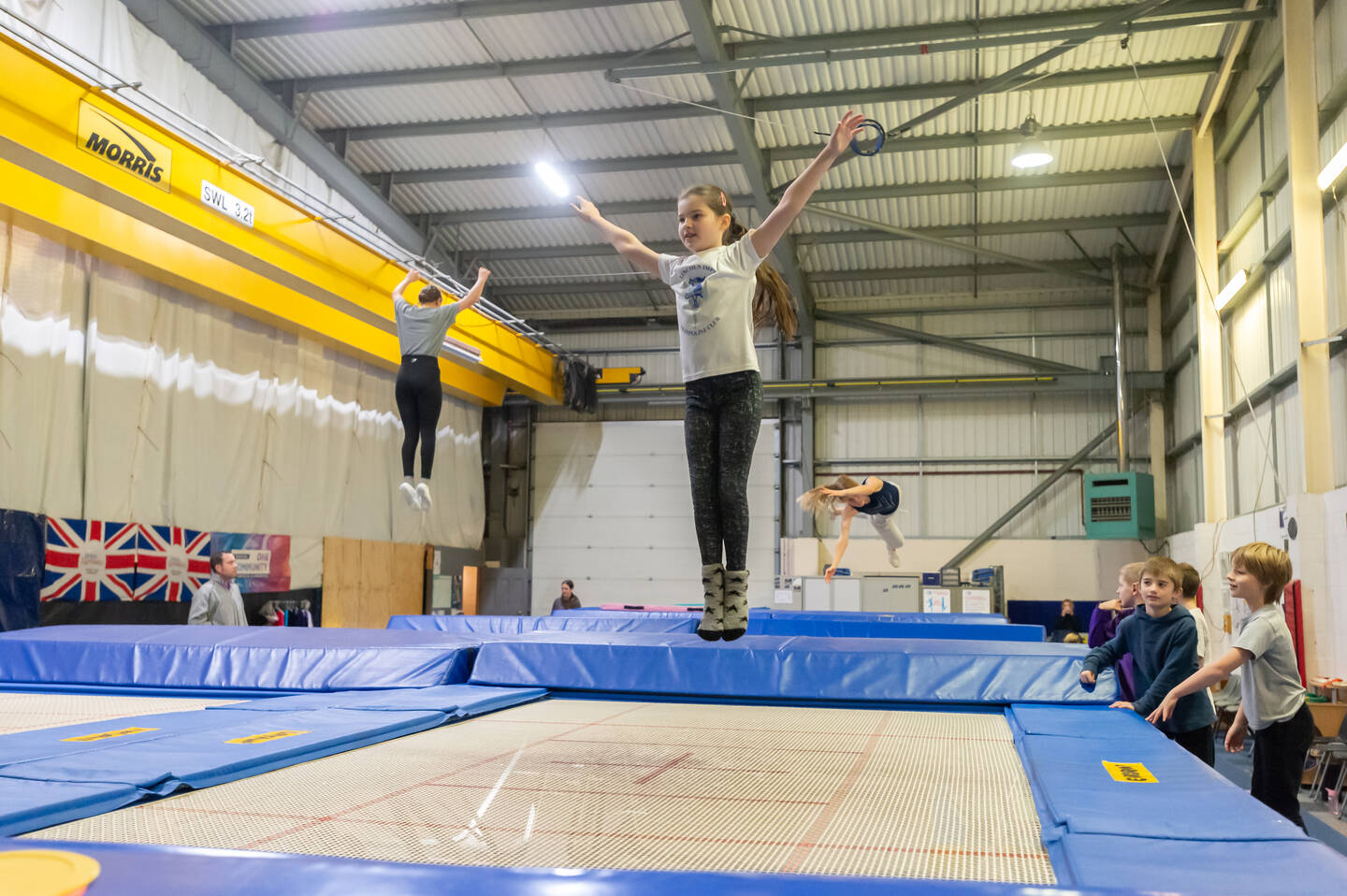 A young girl bounces on a trampoline in a hall with lots of trampolines laid out.