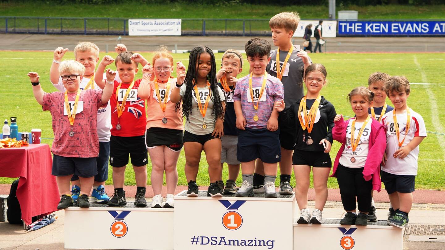 A group of children with dwarfism pose in a group for a photograph at the DSAUK National Games. There is a track behind them.