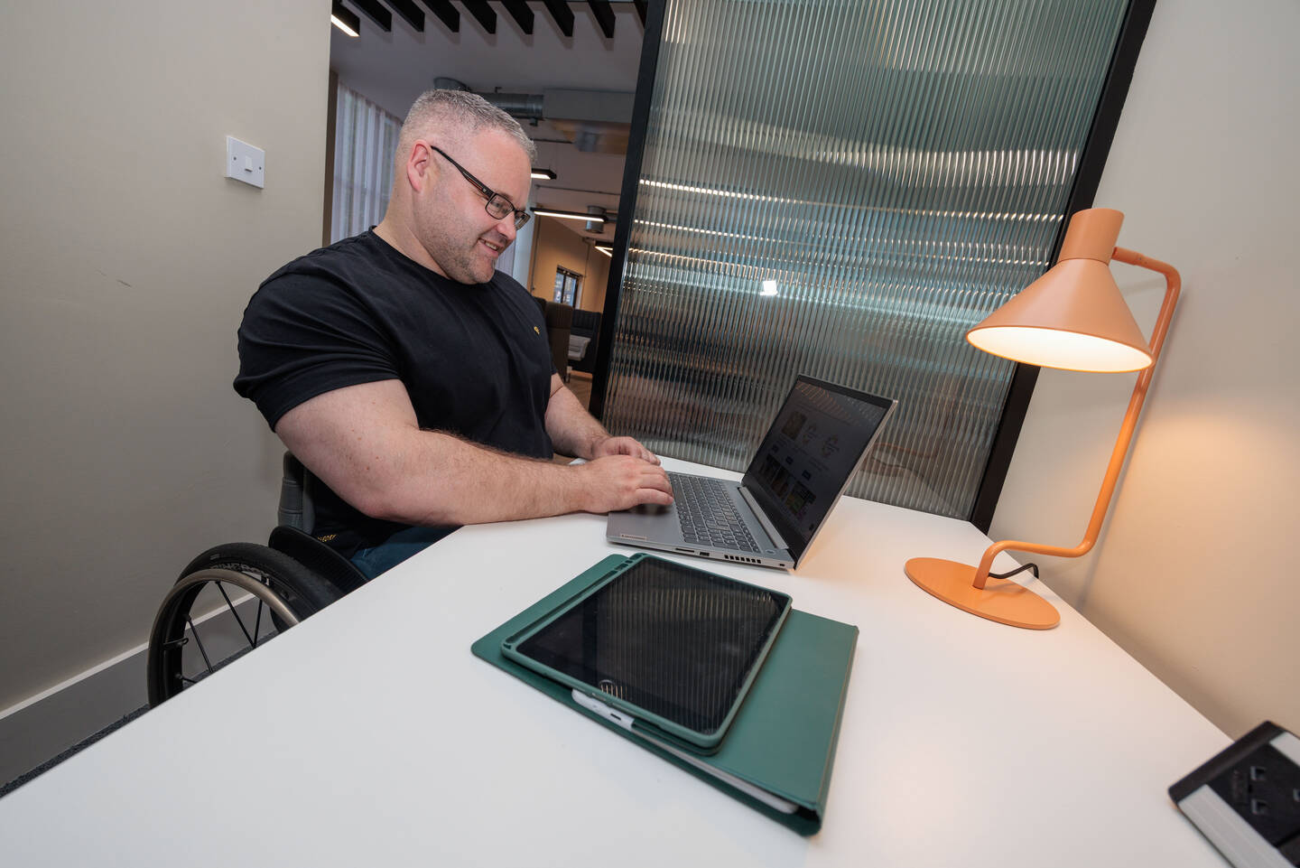 A man using a wheelchair sits in an office using a laptop.