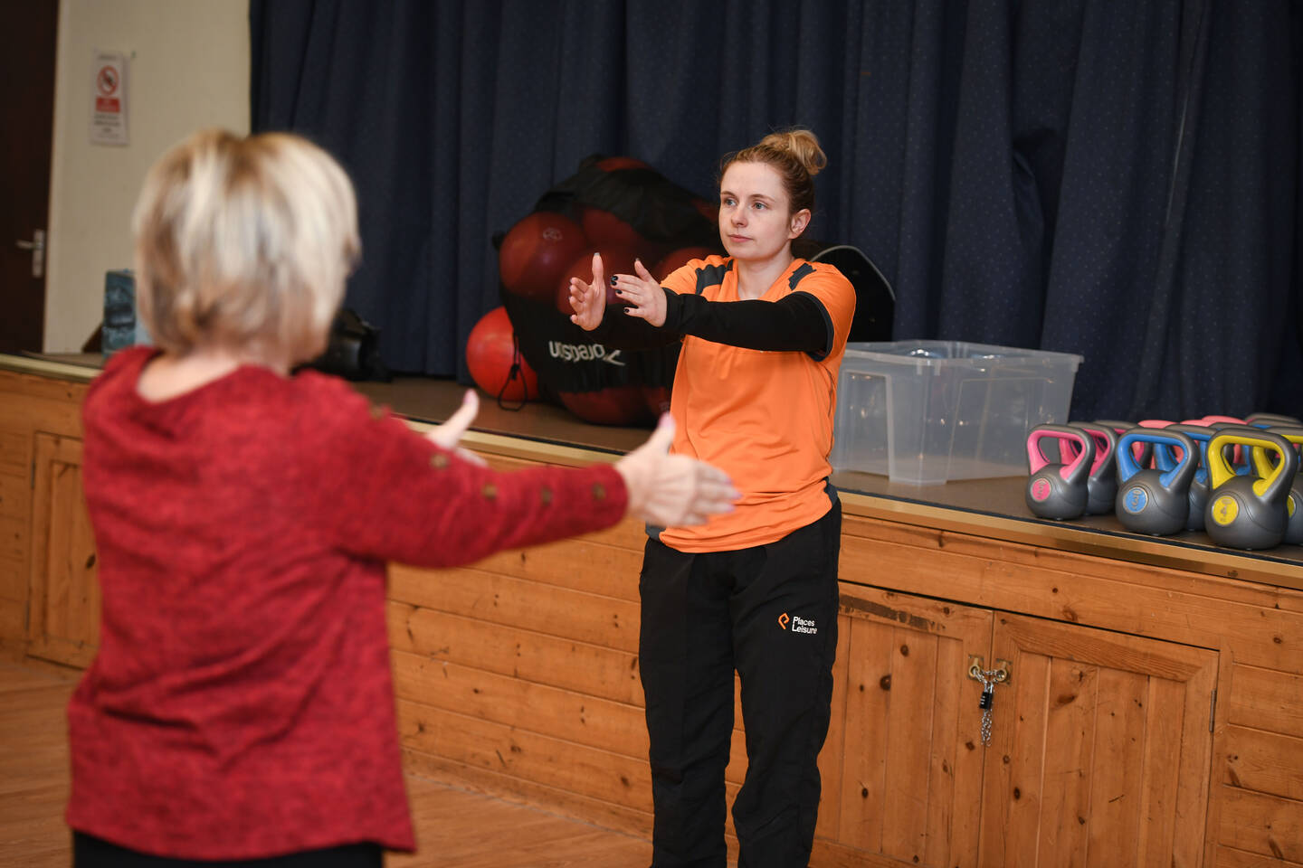 A woman leads an exercise class in a sports hall.