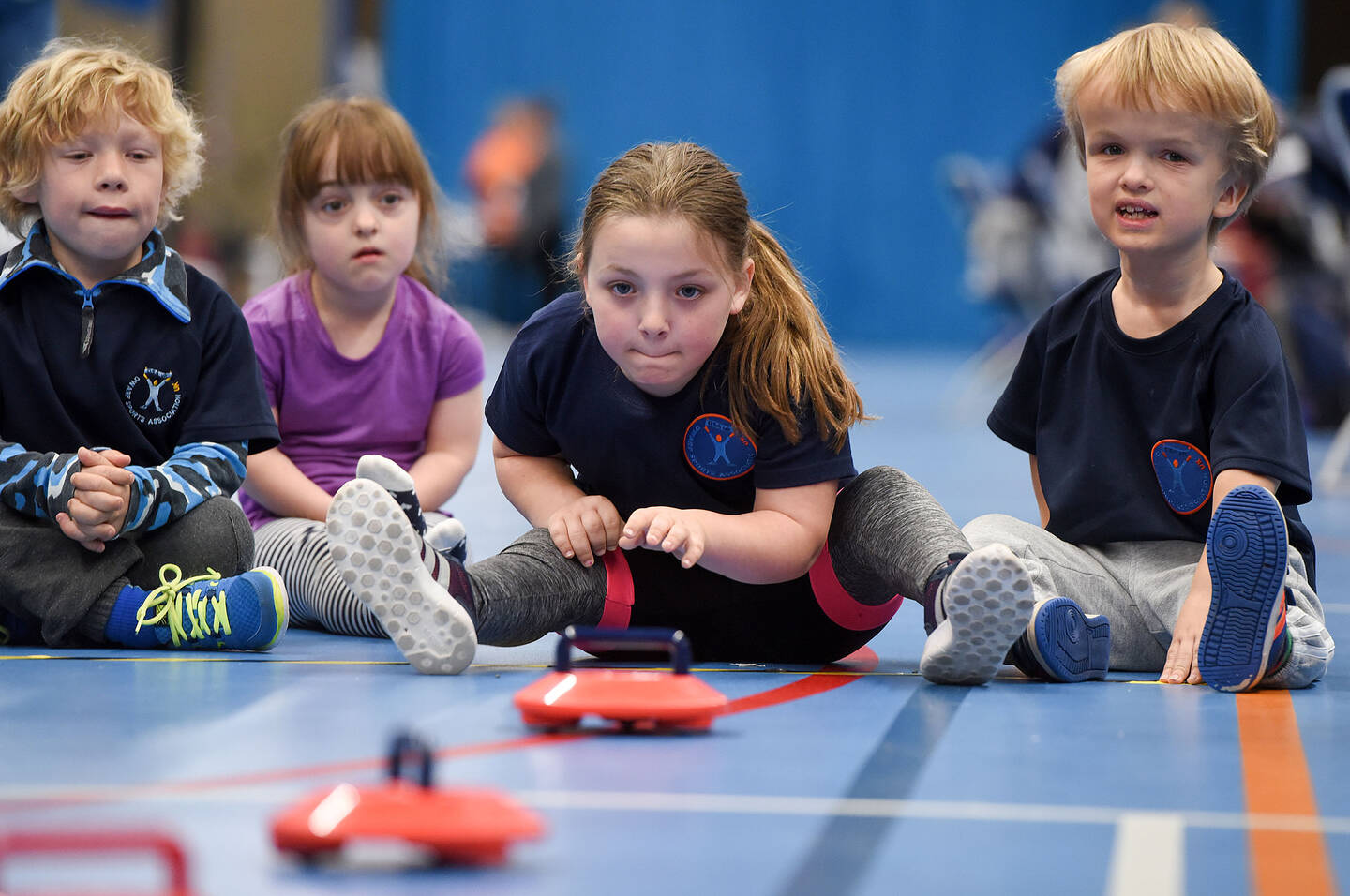 Four children sit on the floor playing a style of curling.