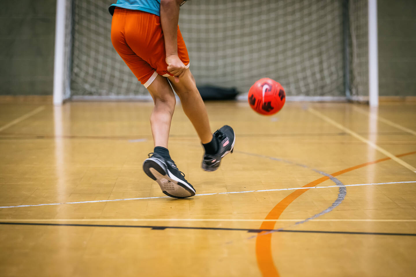 The legs of someone kicking a ball into a net.