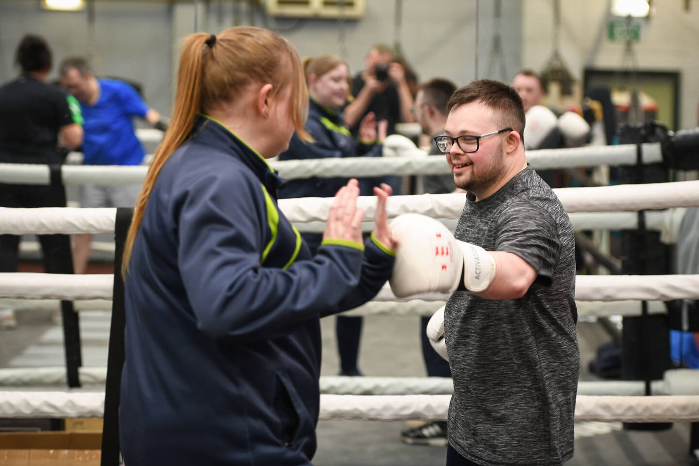 A man in a boxing ring punches the hand of a trainer. 