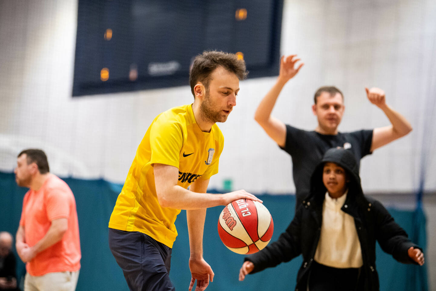 A man in a yellow top dribbles a basketball.