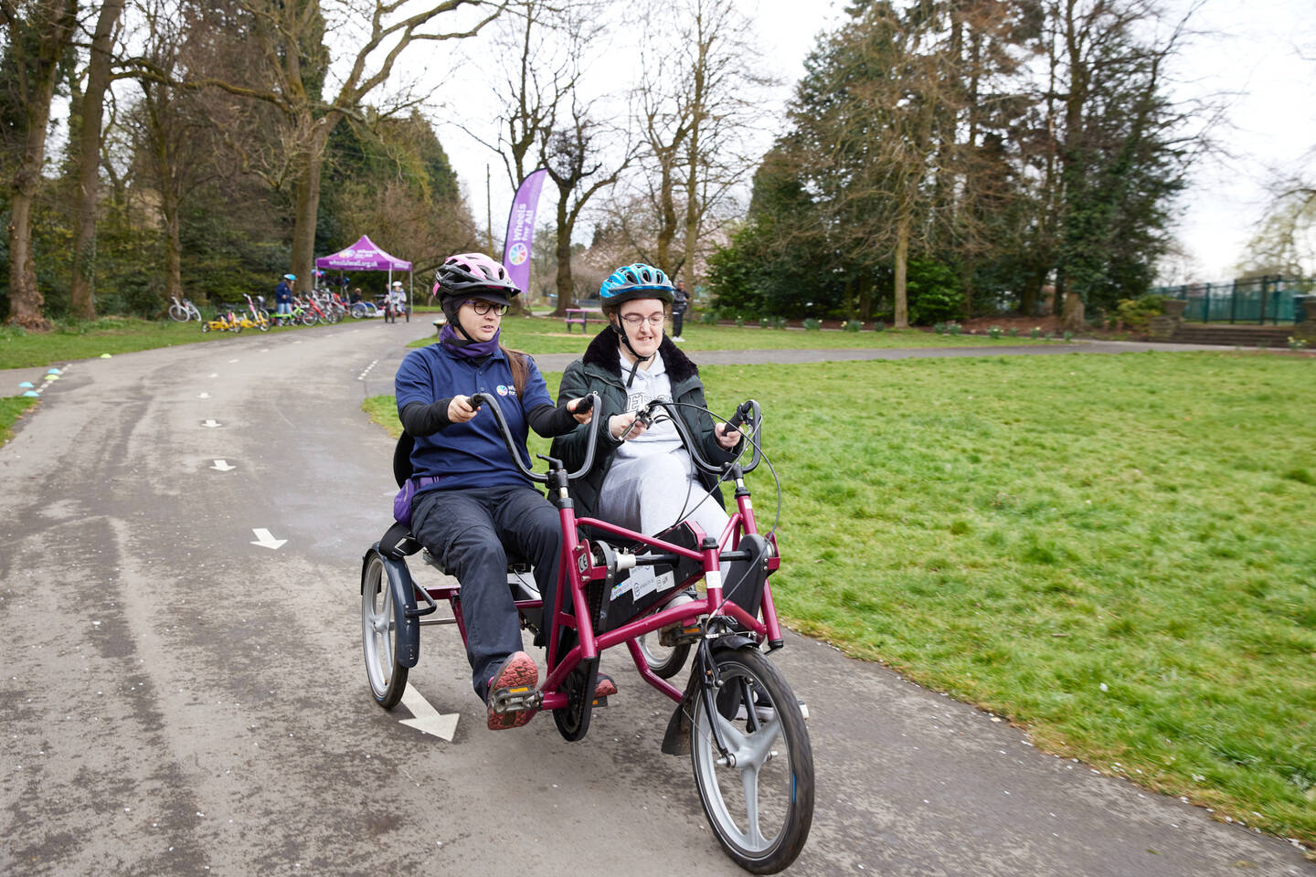 Two people ride an adapted trike in a park.