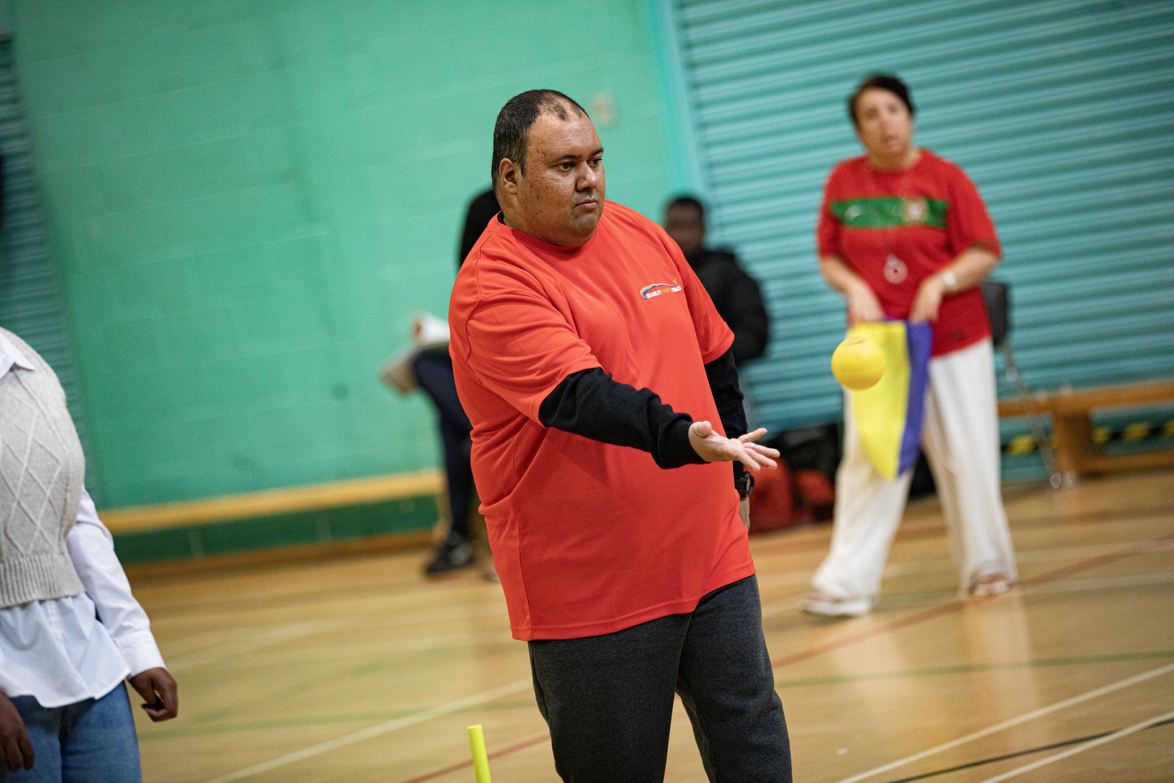 A volunteer for Disability Sports Coach throws a ball in a sports hall.