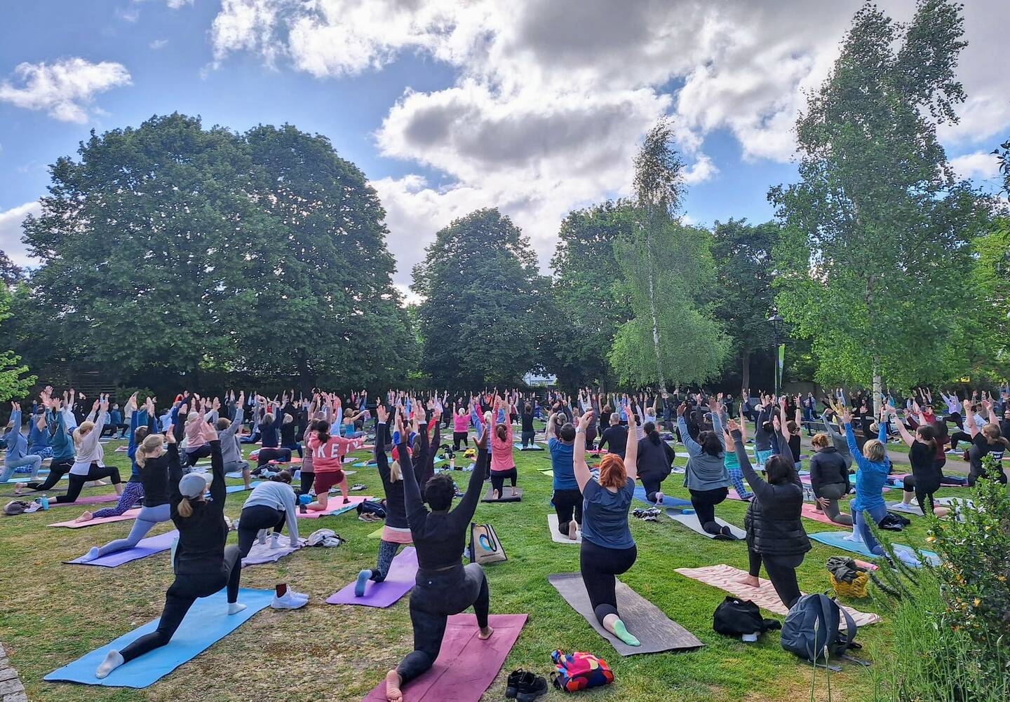 Large group of people kneeling on yoga mats and raising their arms in a park taking part in a Park Yoga session. Photo credit: Park Yoga