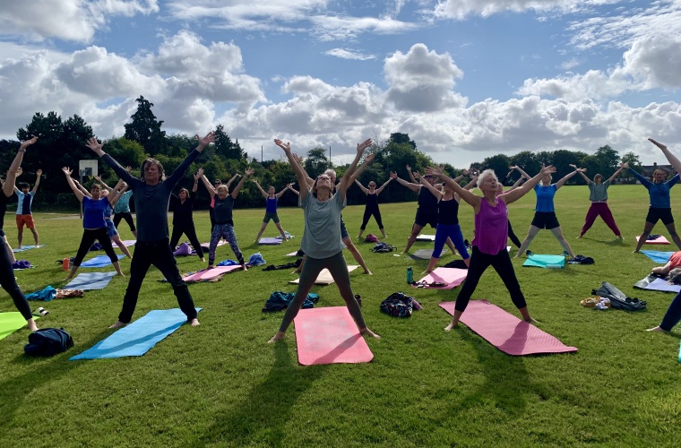 Large group of people standing up on yoga mats with their arms up in the air in the park taking part in a Park Yoga session. Photo credit: Park Yoga.