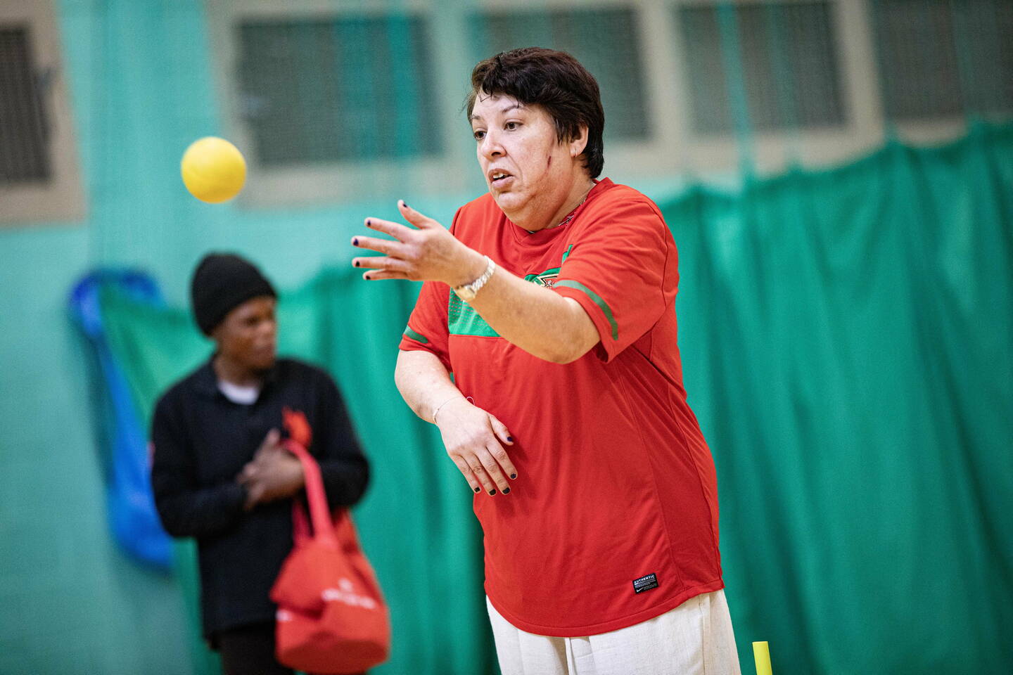 A disabled woman wearing a red t-shirt throws a small ball during an inclusive activity session