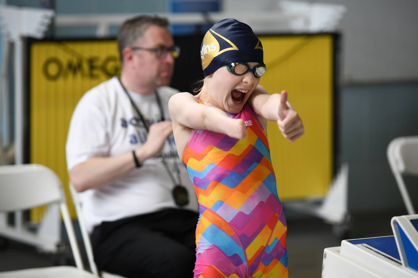 A young swimmer gives a thumbs up by a swimming pool.