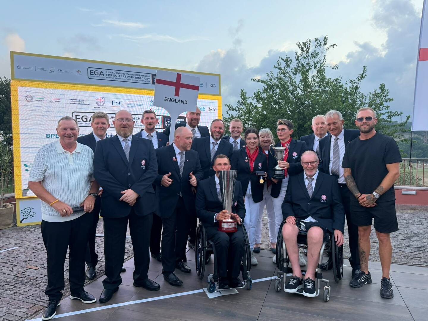 An image showing around 15 people, one holding a trophy. They are wearing suits, with a sign showing they are the England Disability golf squad from 2026 European Championships.