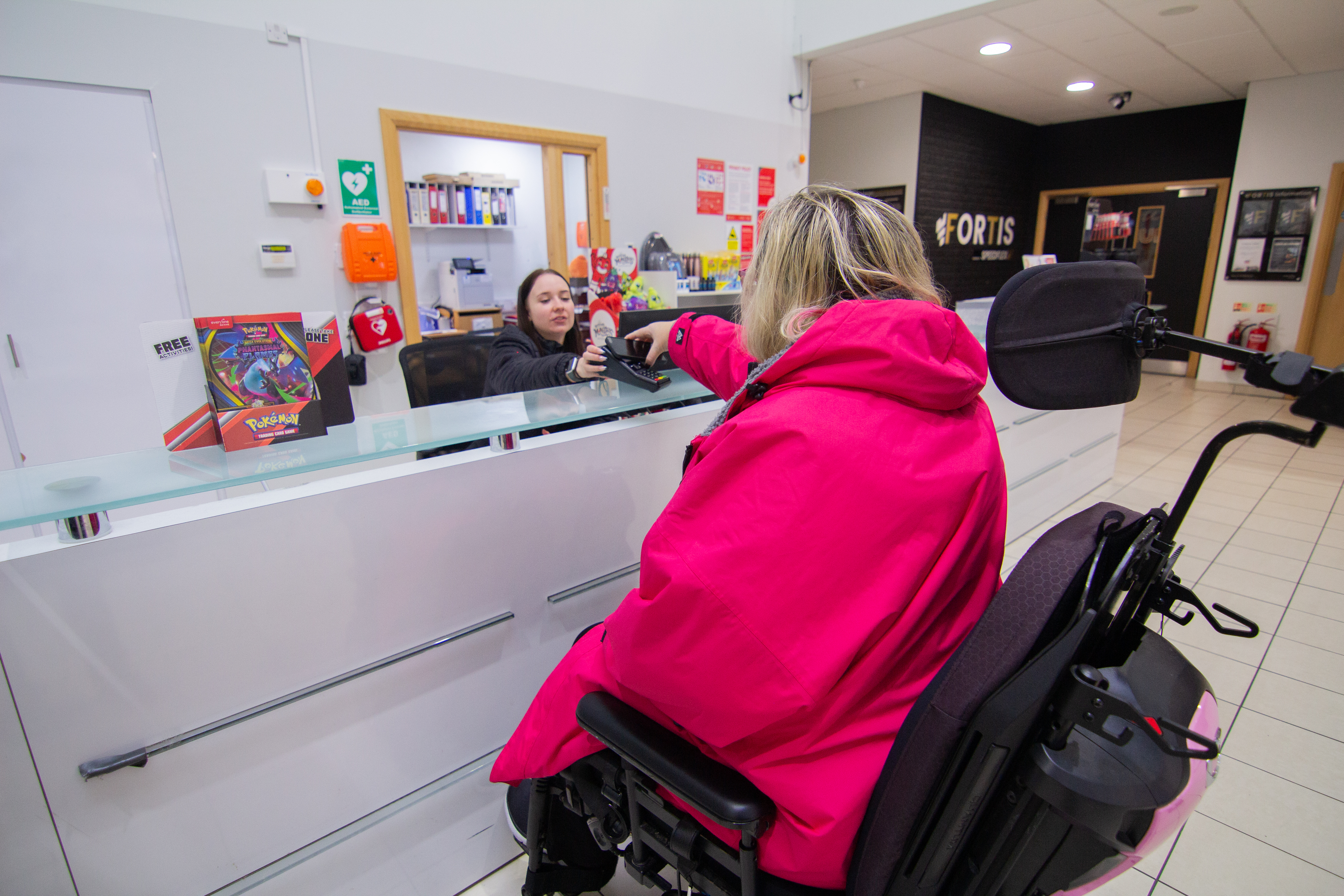 A women using a wheelchair at a gym reception paying for something.