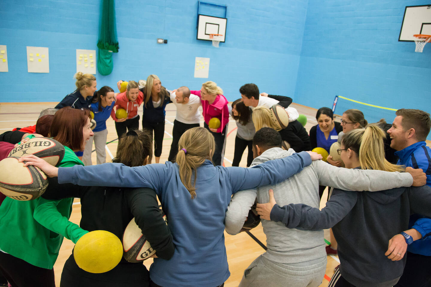 A group of people stand in a sports hall in a huddle.