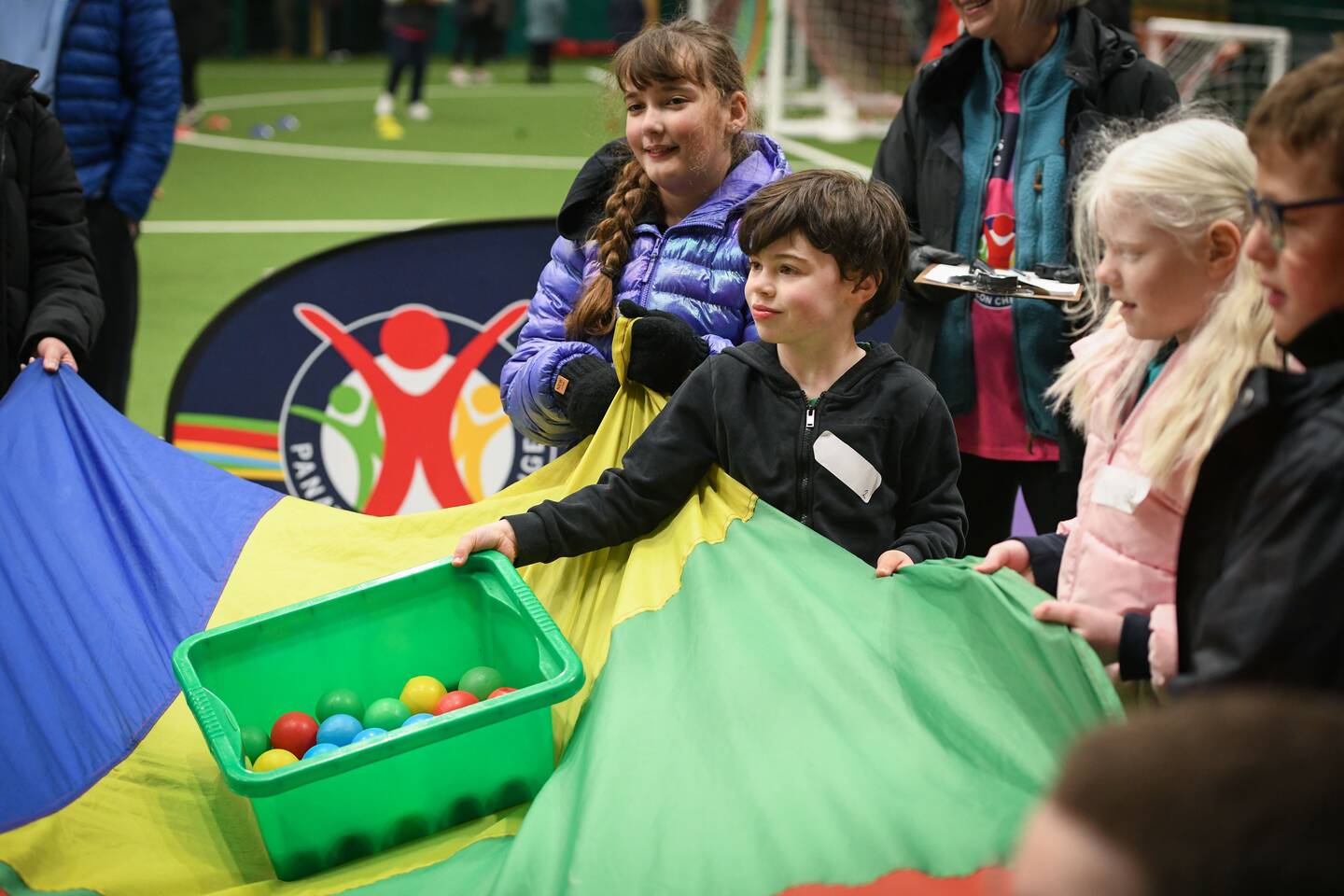 A group of children with a colourful tarp throw a box of balls onto the tarp