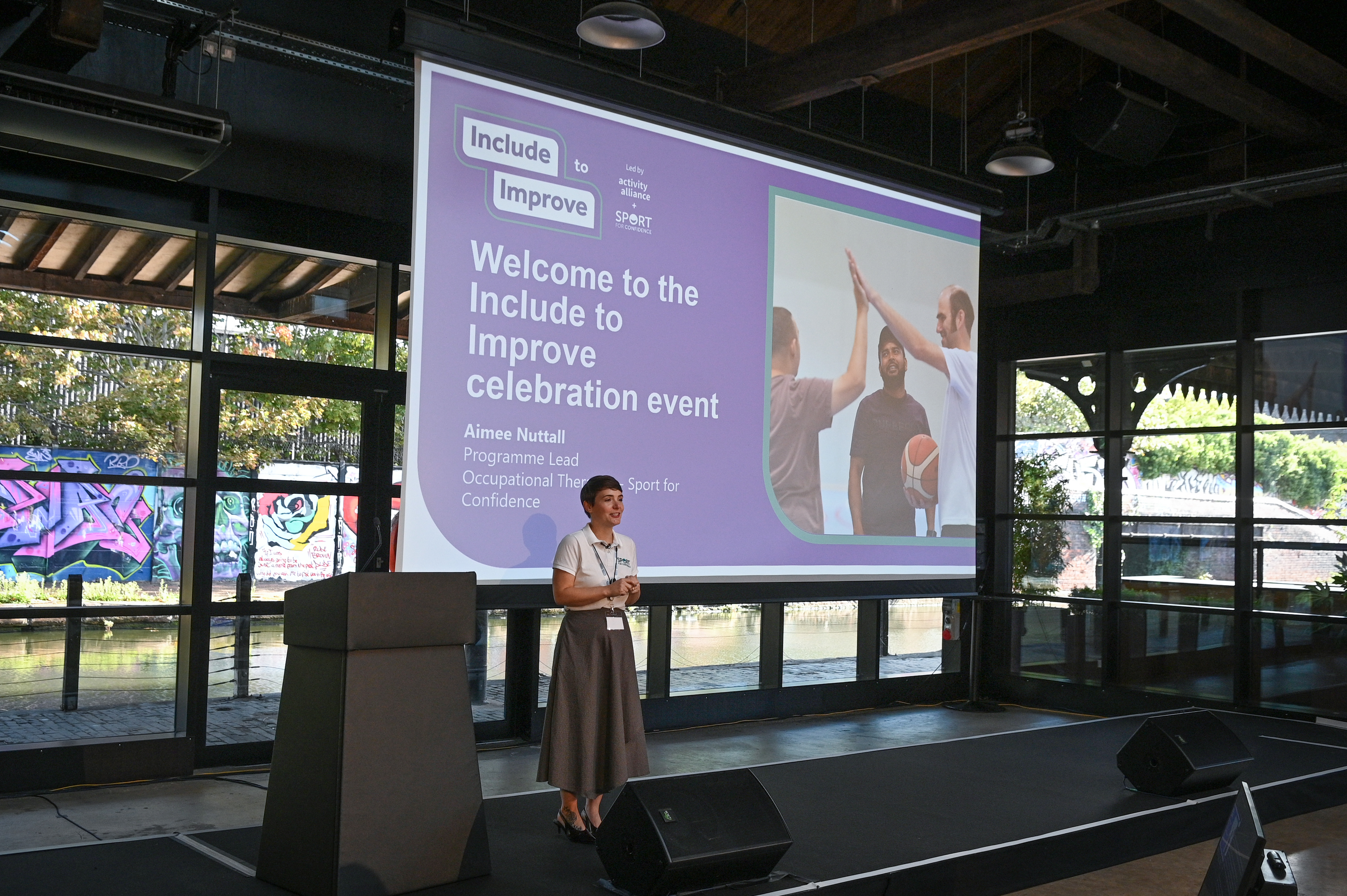 A speaker on stage talking about Include to Improve
